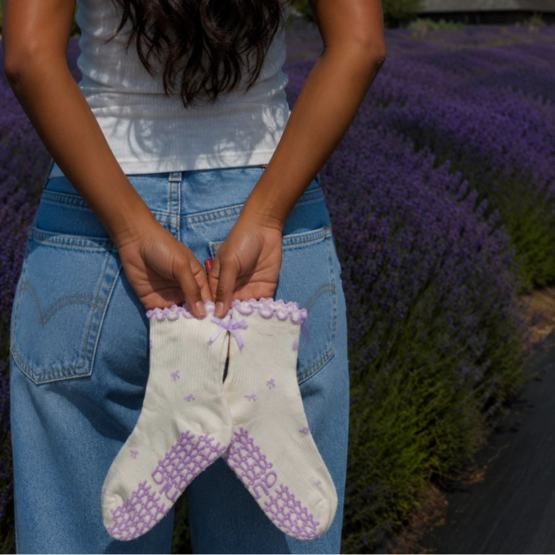 Woman holding lavender bow grip socks with denim jeans in a lavender field