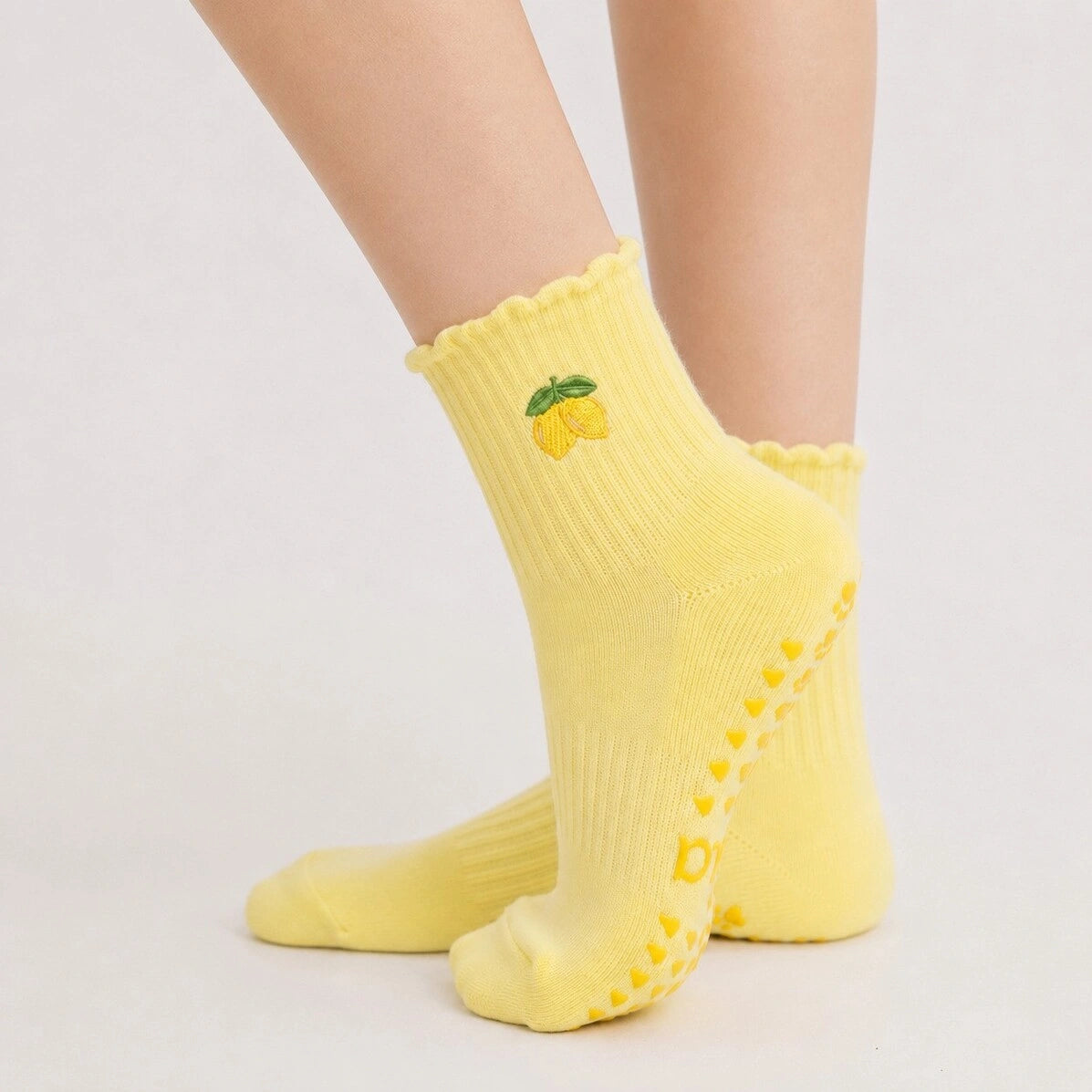 Side view of a bare leg wearing a single yellow lemon-embroidered yoga sock with grips on the sole.