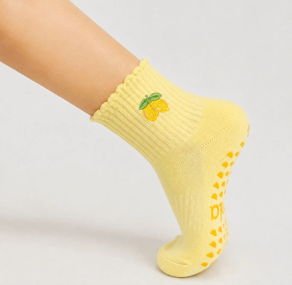 Close-up of a raised foot wearing a yellow lemon-print sock, highlighting its sticky socks barre grip dots.