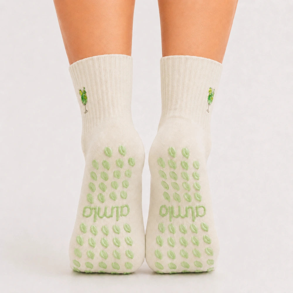 Back view of raised feet wearing cream cocktail-embroidered best grippy socks for barre with green grip dots.