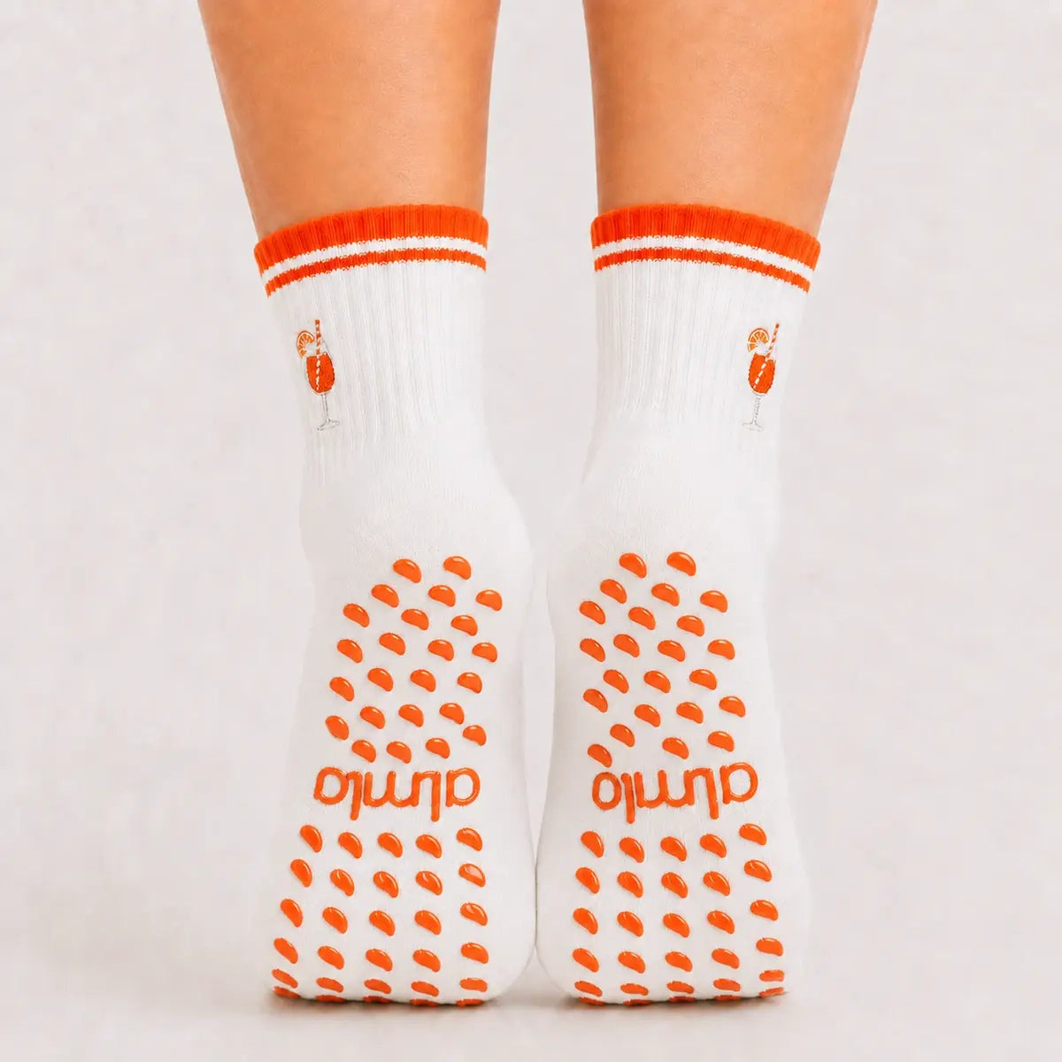 Back view of raised feet wearing white orange-striped grip socks for barre class with cocktail embroidery.