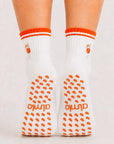 Back view of raised feet wearing white orange-striped grip socks for barre class with cocktail embroidery.