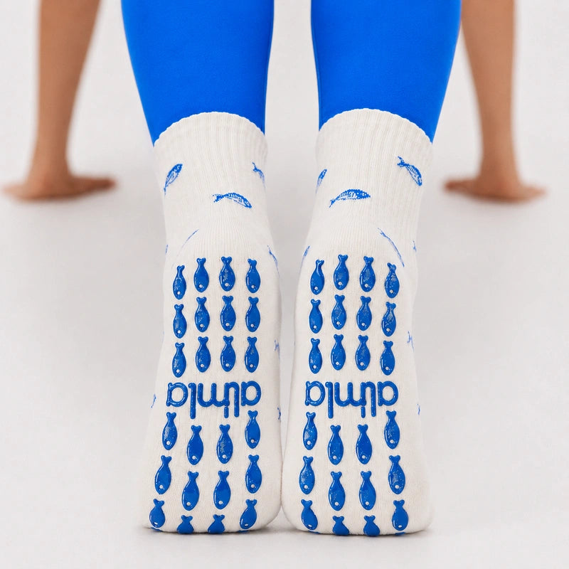 Back view of feet in blue leggings wearing white fish-print non slip yoga socks with blue fish-shaped grips.