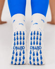 Back view of feet in blue leggings wearing white fish-print non slip yoga socks with blue fish-shaped grips.