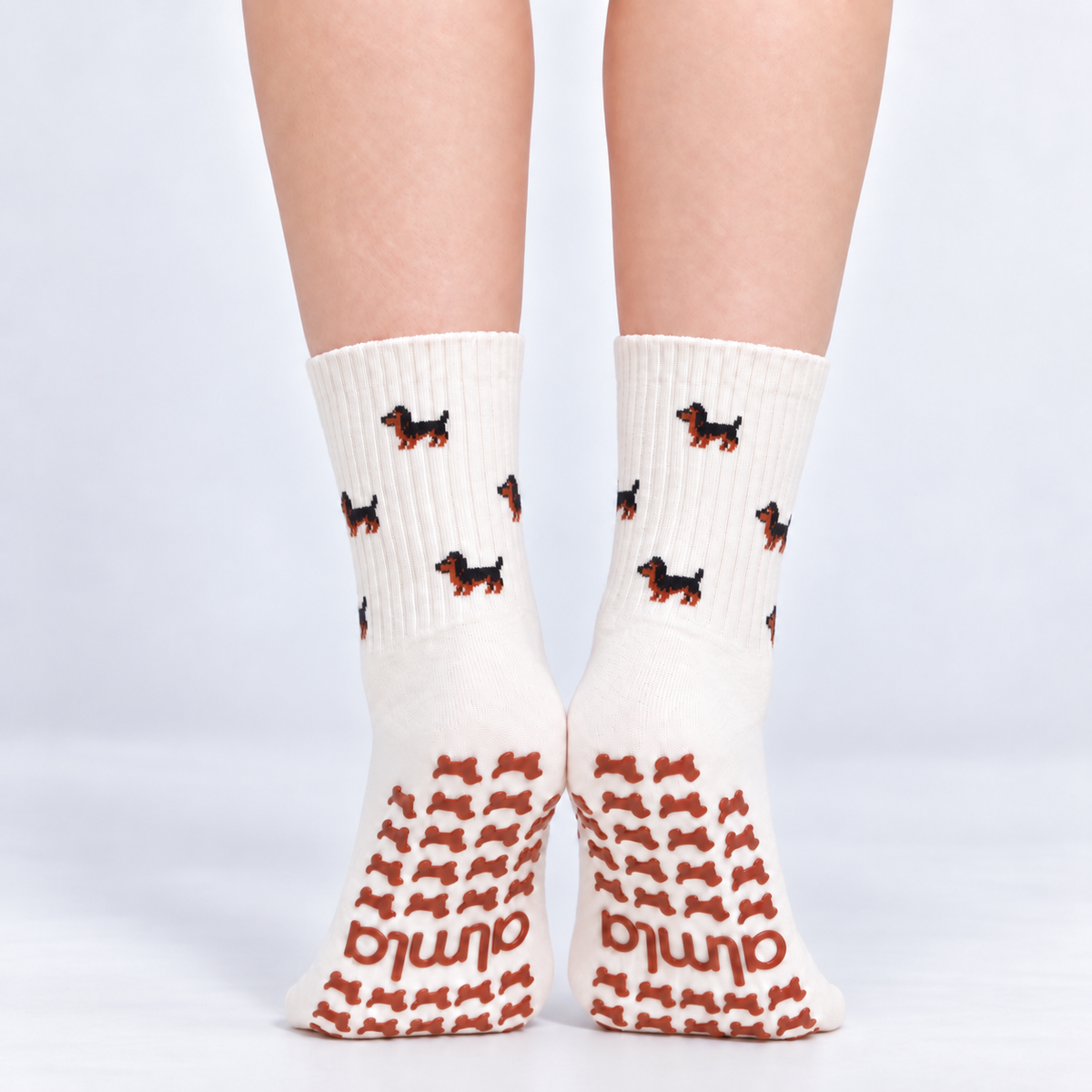 Model standing in a pair of The Dachshund Grip Sock, front view showing the dachshund print and dachshund-shaped grip soles with the Almla logo