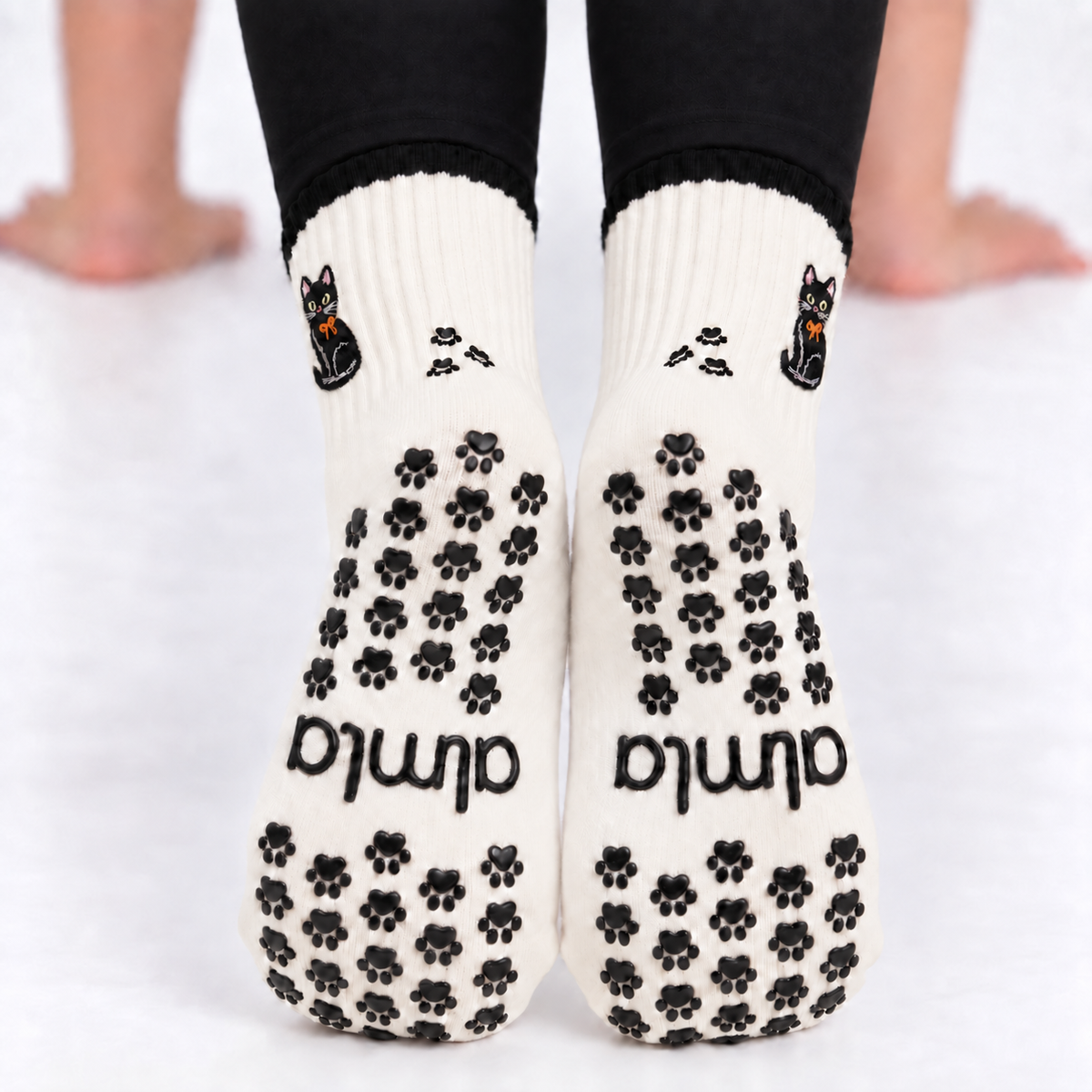 Close up of the soles of the Black Cat Grip Socks with black paw-shaped non-slip grips and almla logo