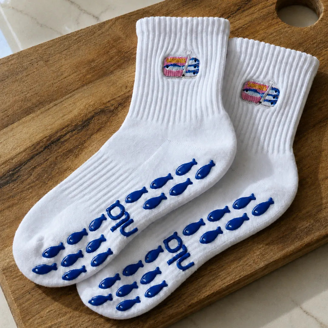 White sardine-tin embroidered barre grip socks with blue fish-shaped grips arranged on a wooden board.
