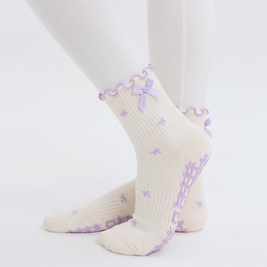 Cream bow print pilates grip socks with lavender ribbon cuff worn with white leggings