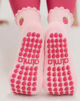 Underside of both feet raised showing pink strawberry best grip socks pilates with pink silicone grip pattern.
