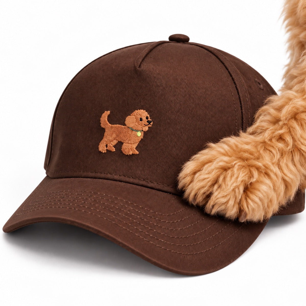 Fluffy goldendoodle paw resting on The Goldendoodle Brown Hat, close up of the embroidered goldendoodle