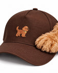 Fluffy goldendoodle paw resting on The Goldendoodle Brown Hat, close up of the embroidered goldendoodle