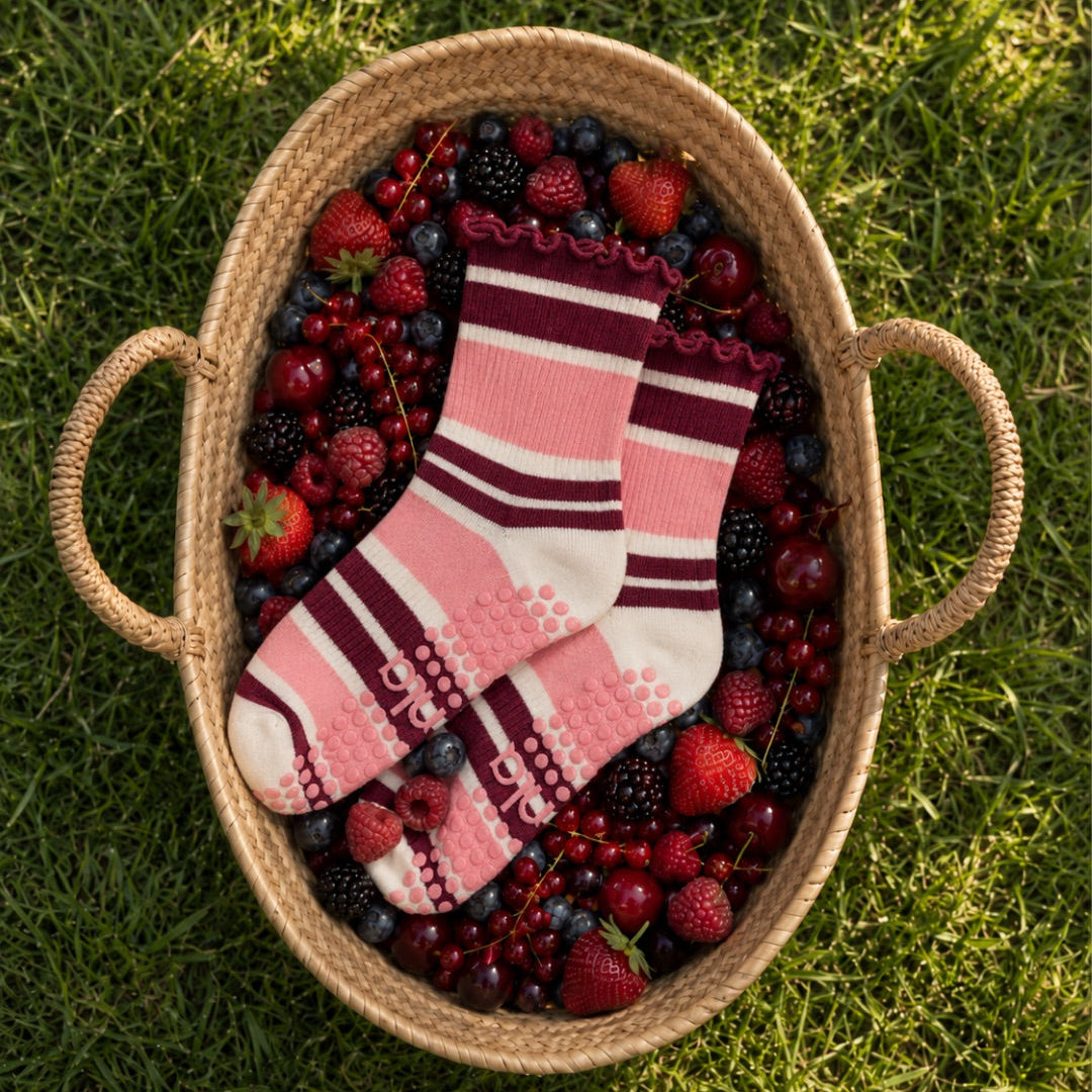 Raspberry cream striped grip socks styled in a basket of fresh summer berries