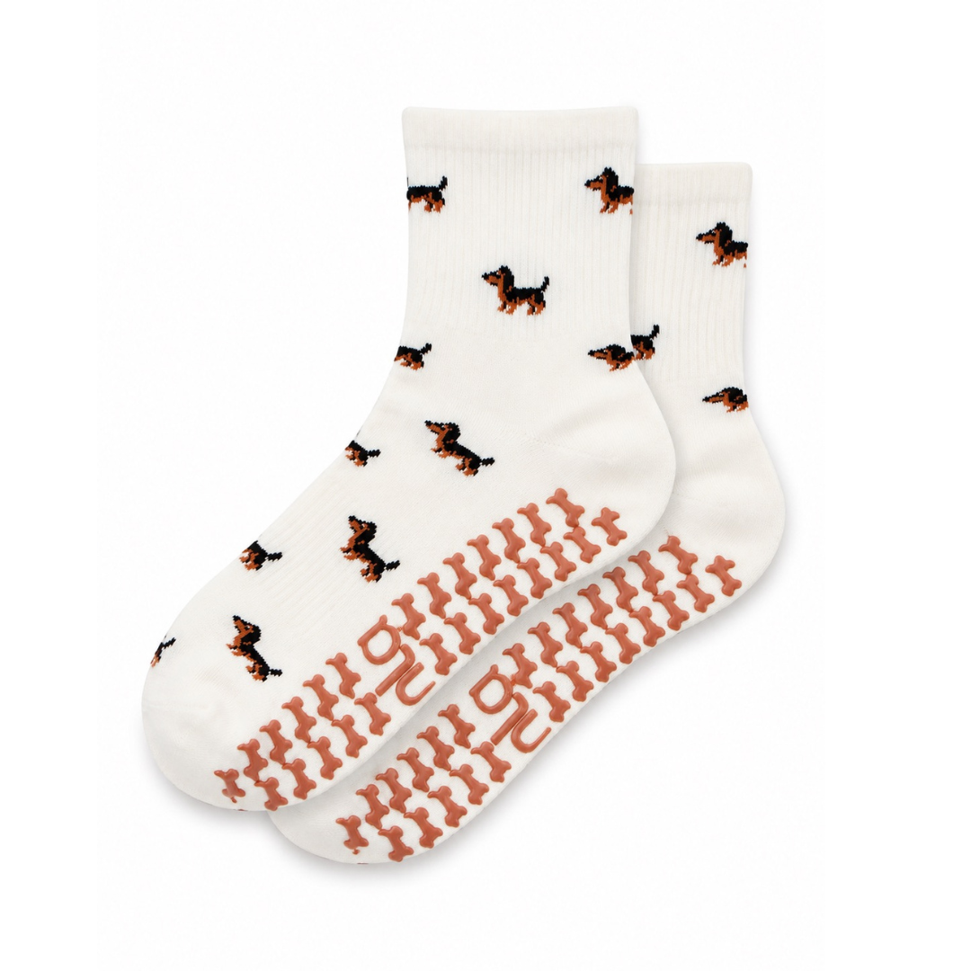 The Dachshund Grip Sock in oat milk with an all-over dachshund print and dachshund-shaped non-slip grips, laid flat on a white background
